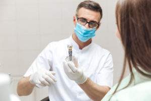 Dentist explaining dental implant model to female patient 