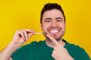 young man smiling and holding Invisalign aligner